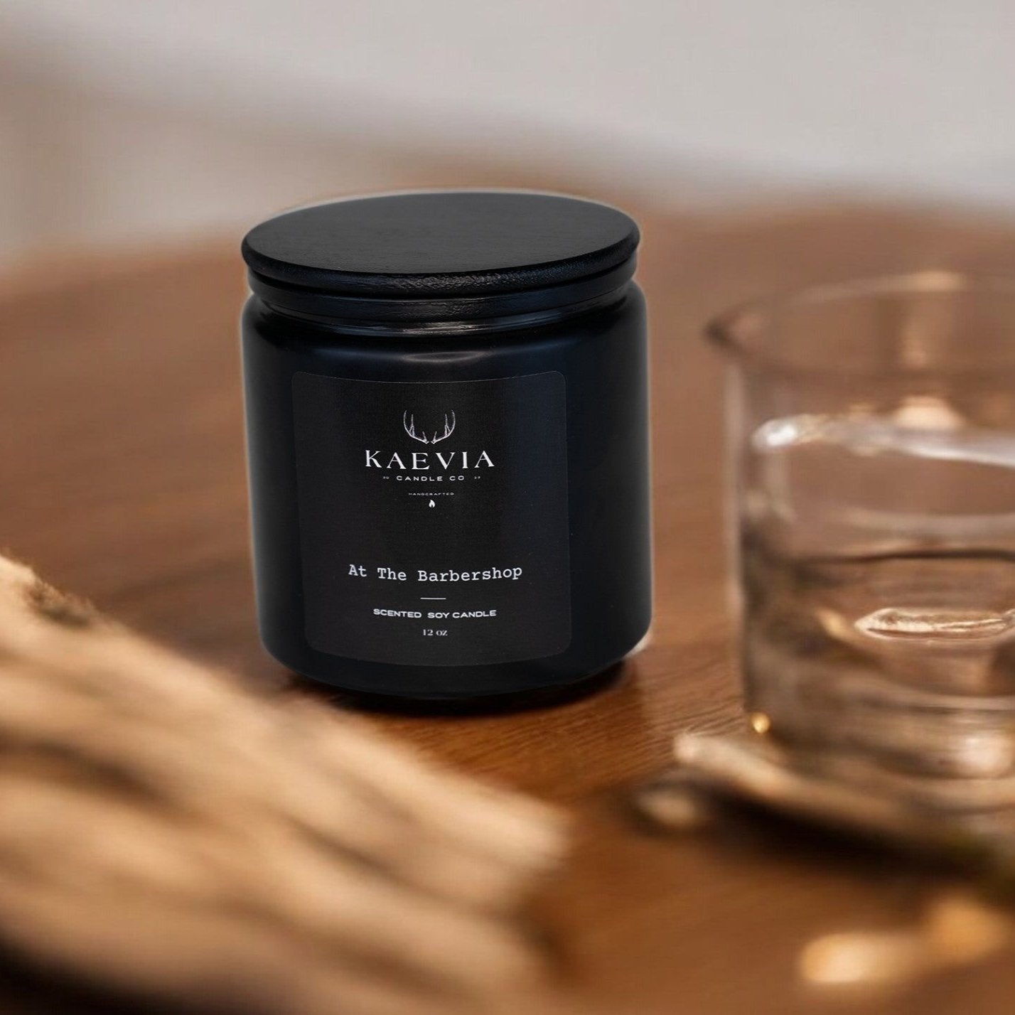 Red Stag 12 point candle in a black jar with a black lid resting on a table with a glass nearby.
