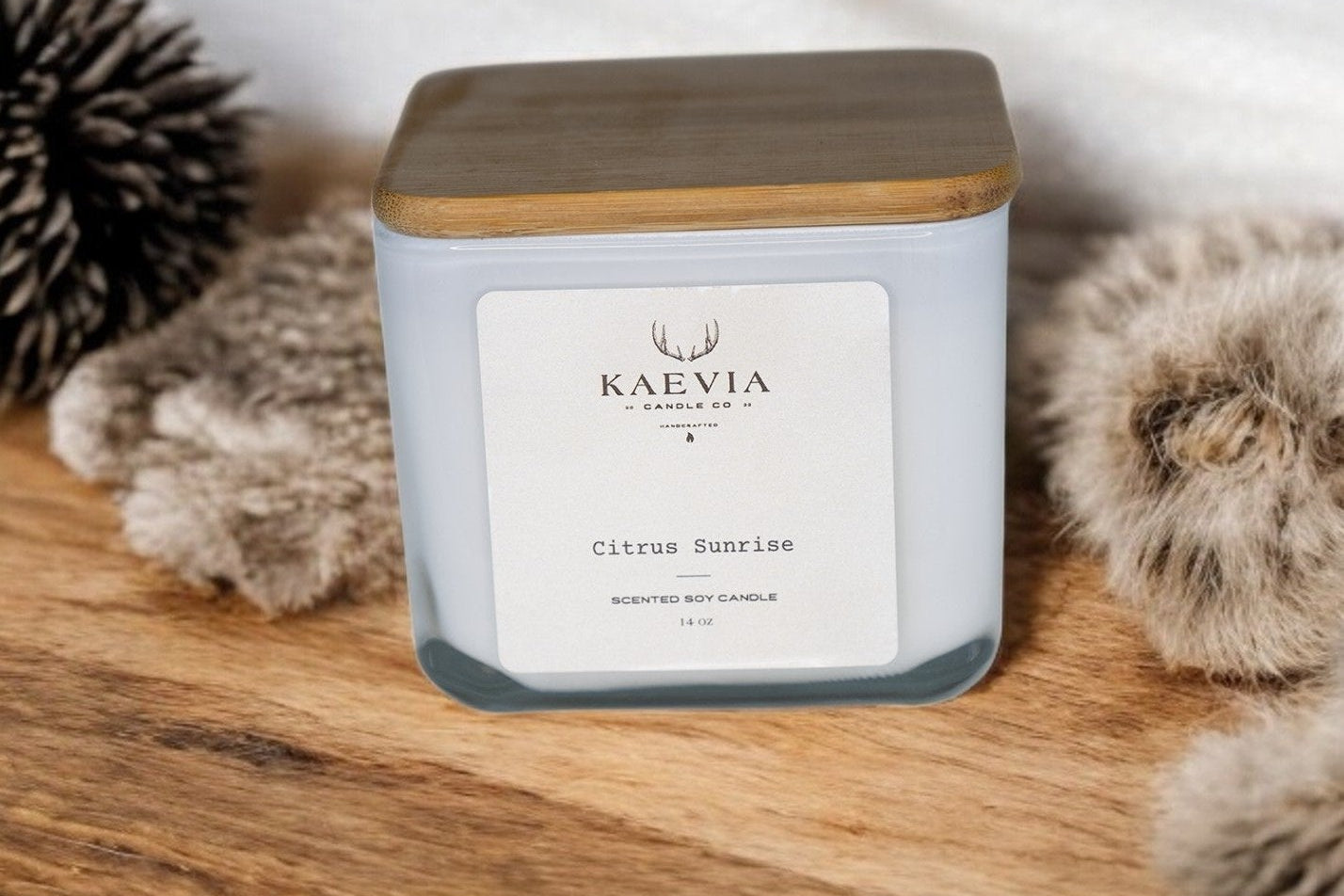 14oz cube candle in white jar with a wooden lid sitting on a table with decorative material