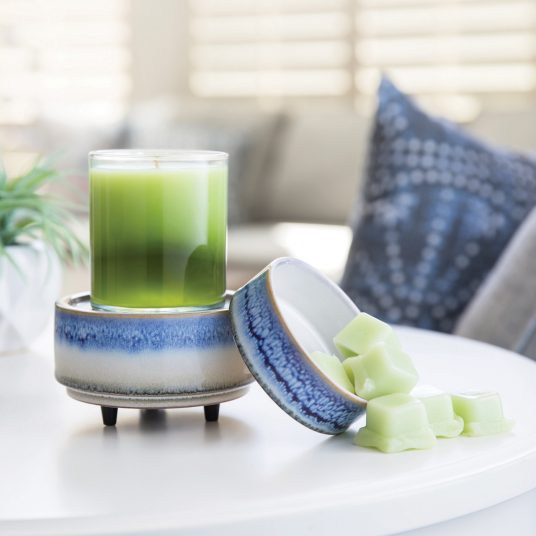 Candle sitting on the candle warmer with melts on the melt tray.  Warmer on a white table. 