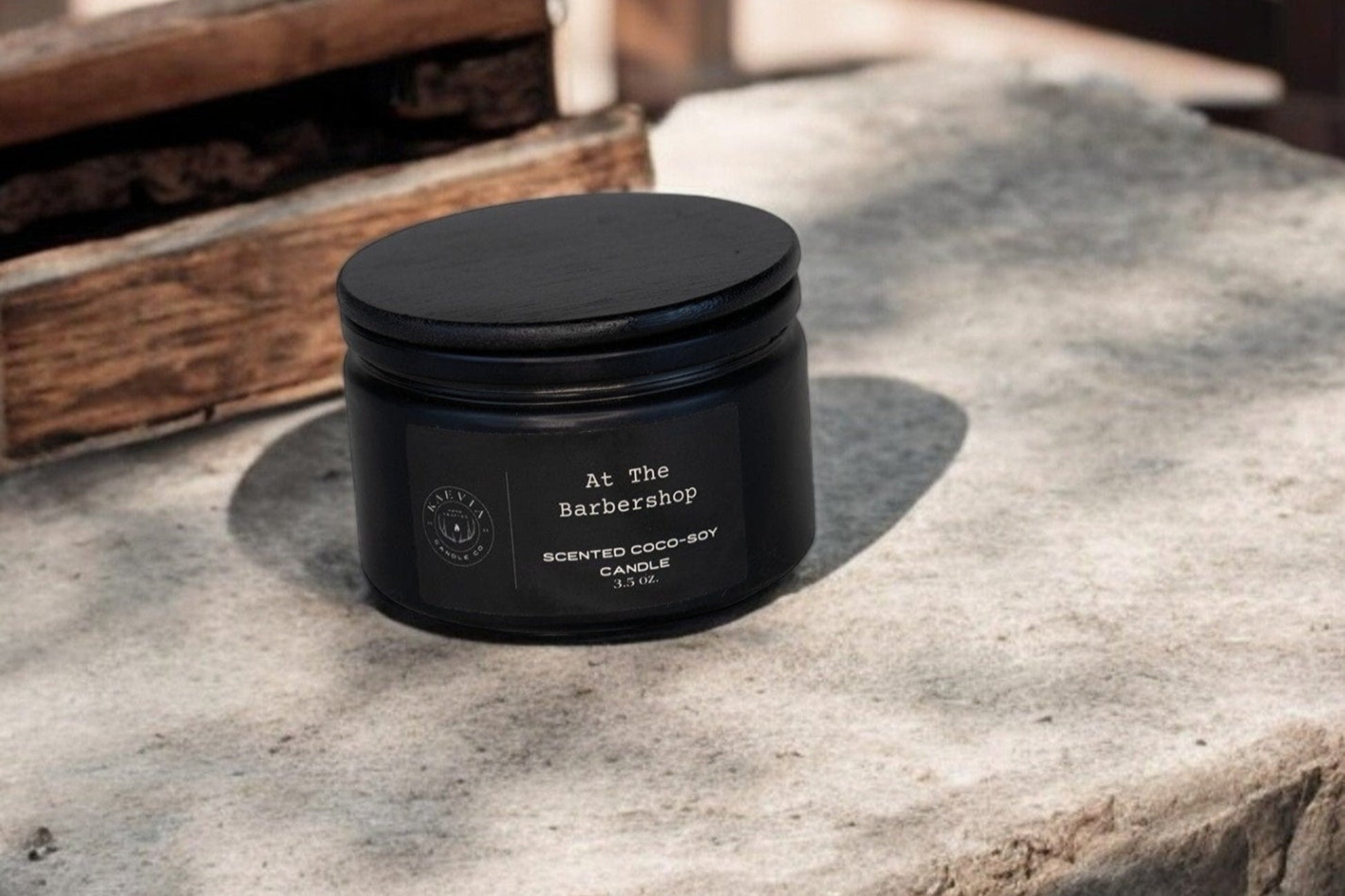 Red Stag Button Buck coconut-soy At The Barbershop candle scent in a black jar with a black lid on concrete